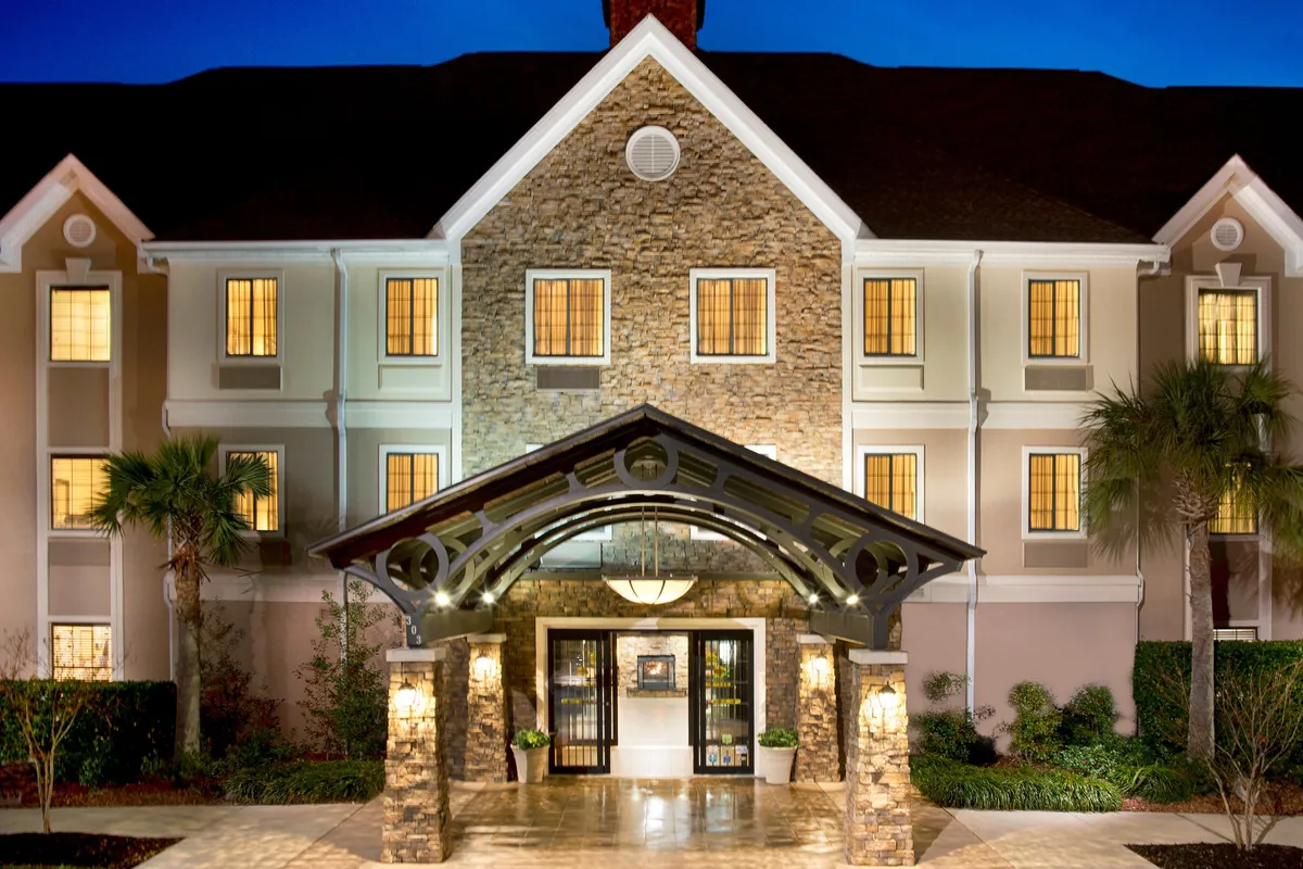 The image presents the welcoming arched entrance of Staybridge Suites Myrtle Beach-Fantasy Harbour, featuring a stone facade and warm, illuminated windows. The inviting exterior hints at comfort and hospitality, setting a positive first impression for business travelers arriving at the hotel.