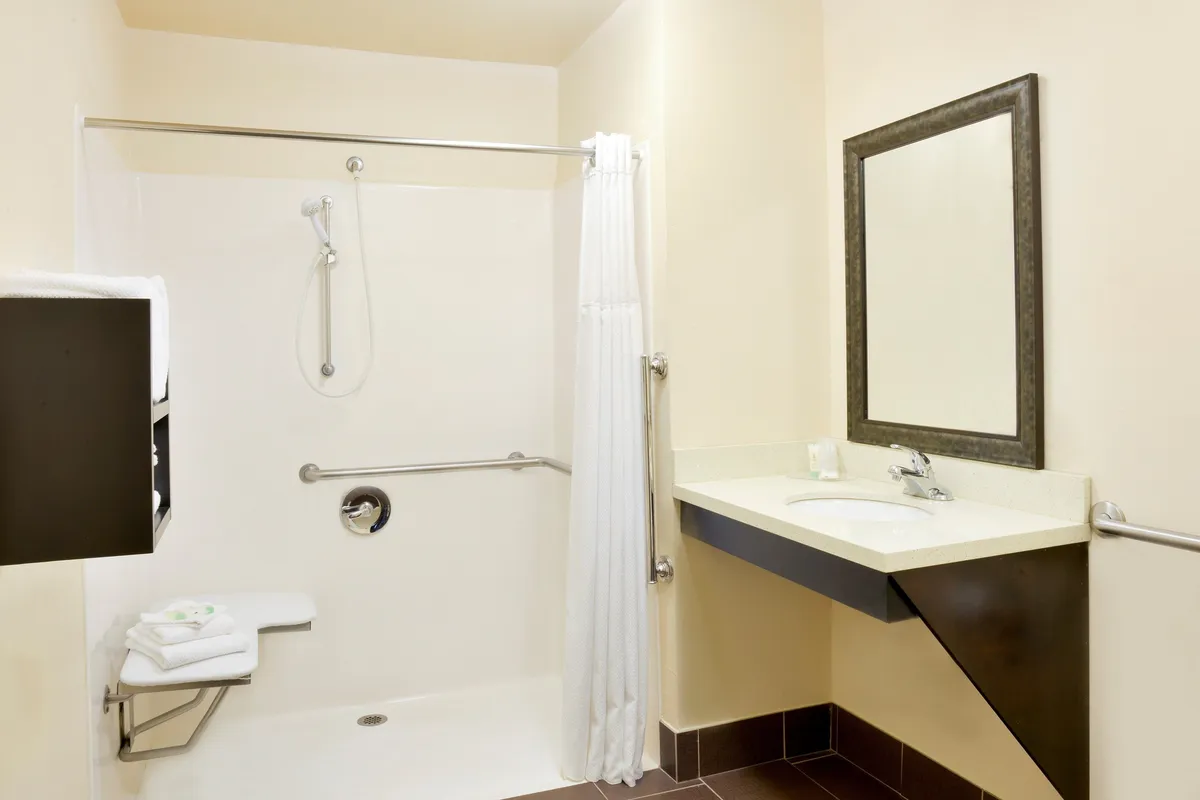This image captures a fresh and inviting bathroom interior, featuring a walk-in shower area, a sink with a large mirror, and plush towels neatly arranged. The space is designed for both functionality and comfort, setting the tone for a relaxing and private retreat.