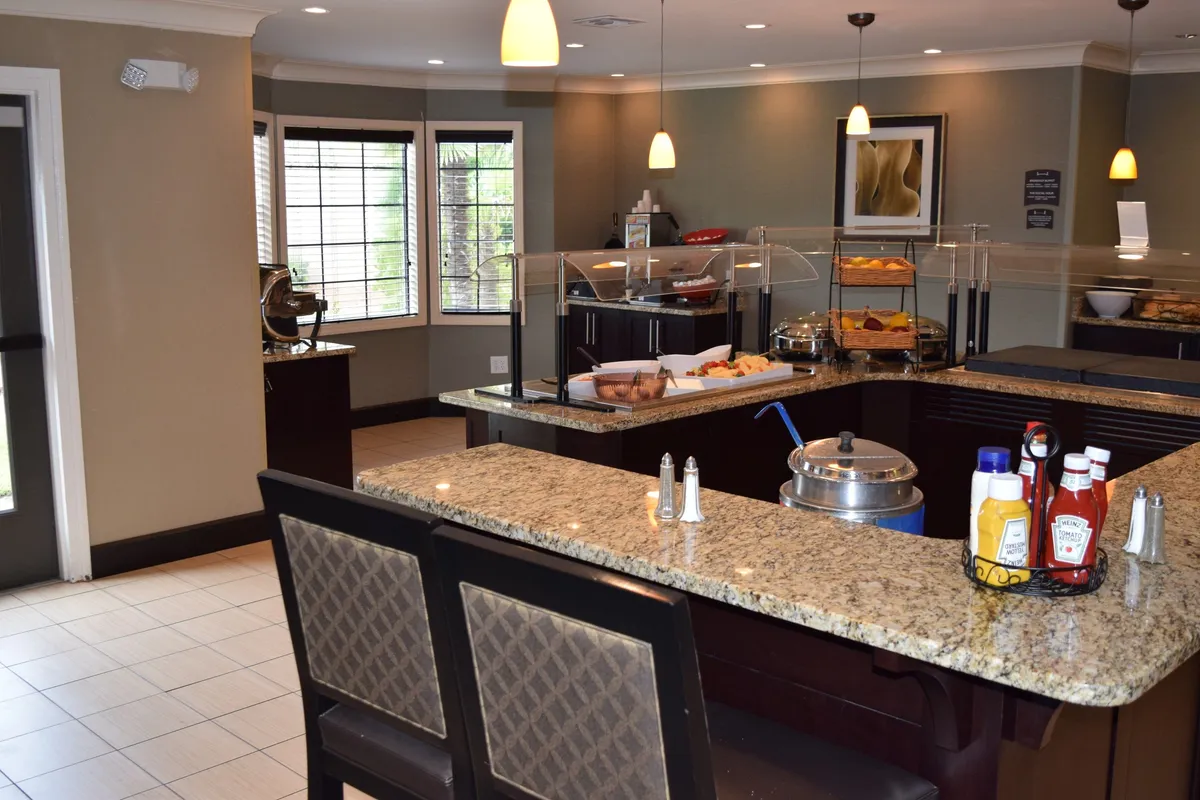 This interior shot captures a granite countertop set for casual dining, with bar stools and window seating in view. Food is displayed on the counter, suggesting a relaxed, independent mealtime experience. The space feels inviting and adaptable—ideal for guests preparing their own meals or enjoying a leisurely breakfast.